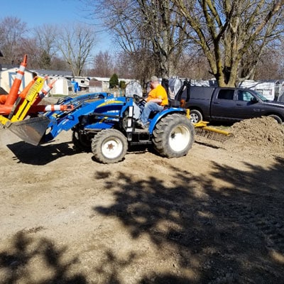 DisplayMax construction worker using a blue tractor to clear and level dirt at an active worksite.