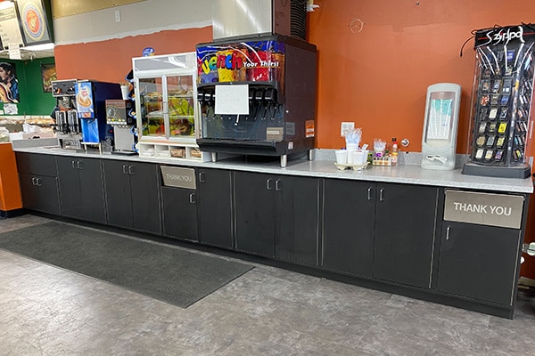 A design of a straight retail counter featuring integrated cup holders, condiment stations, trash and napkin dispensers, storage cabinets.